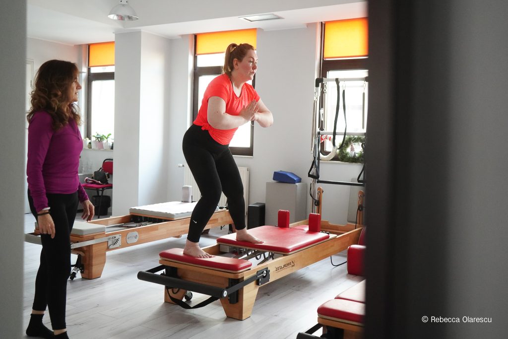 Mirela Olarescu urmărește o clientă care lucrează pe Pilates Reformer, în studioul M.Therapy